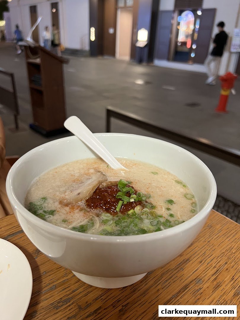A close-up of a steaming bowl of ramen with pork, chili paste, and green onions.