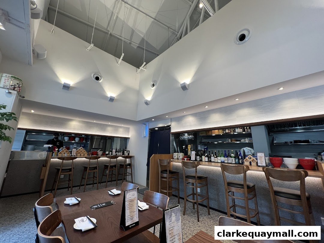 Interior of a modern Japanese restaurant with a bar, tables, and a view of the kitchen.