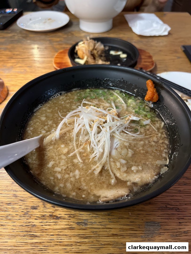 A close-up of a steaming bowl of ramen with pork, green onions, and a dollop of chili paste.