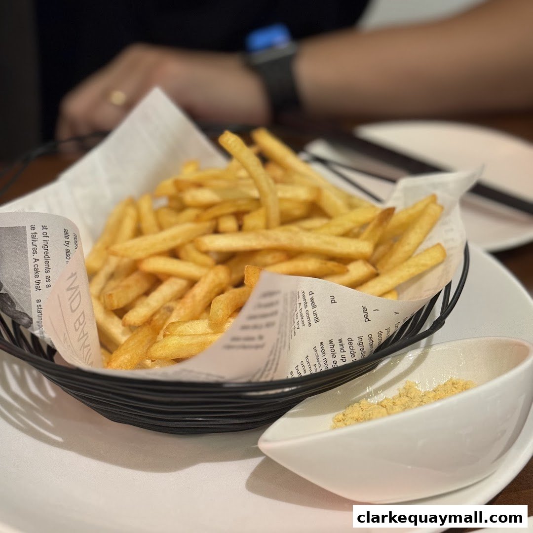 A basket of golden french fries served with a small dish of seasoning.