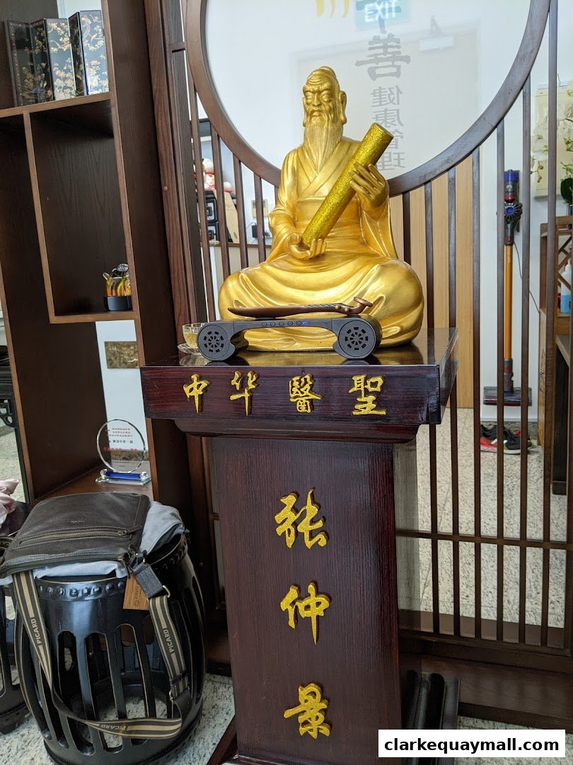 A golden statue of a wise figure holding a scroll, displayed in a shop with traditional decor.