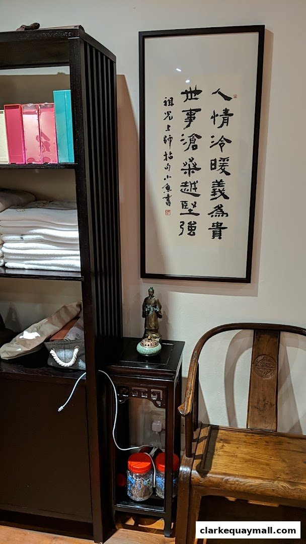 A room with a bookshelf, a framed calligraphy, a statue, and a wooden chair.