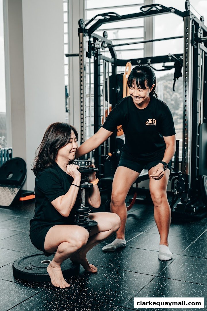 A trainer assists a client with a dumbbell squat in a gym.