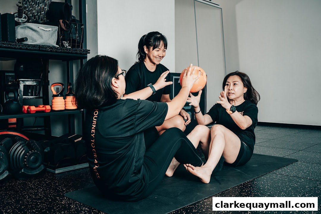 Three women in a gym setting are engaged in a fitness activity, passing a medicine ball.