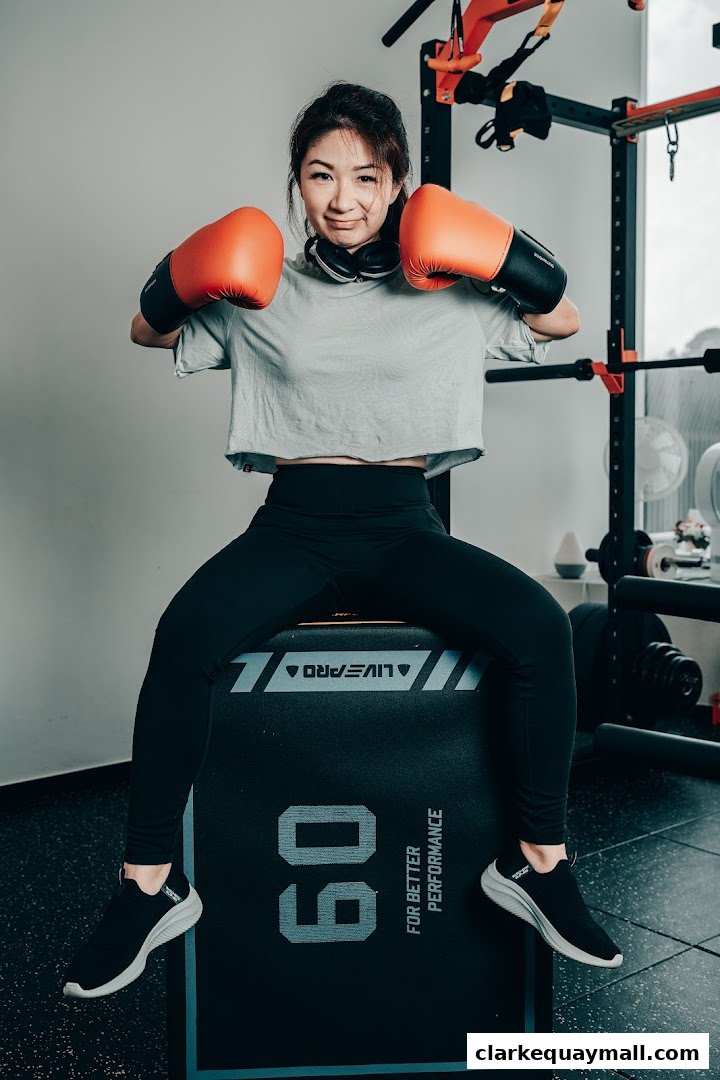 A woman in boxing gloves sits on a plyometric box in a gym.
