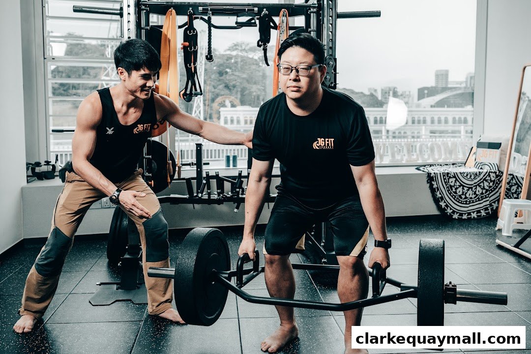 A trainer assists a client with a hex bar deadlift in a gym.
