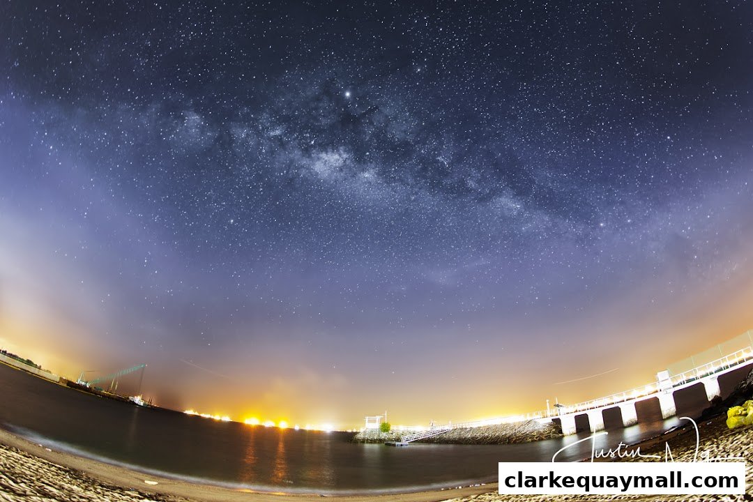 A stunning night sky with the Milky Way over a calm sea and illuminated coastline.