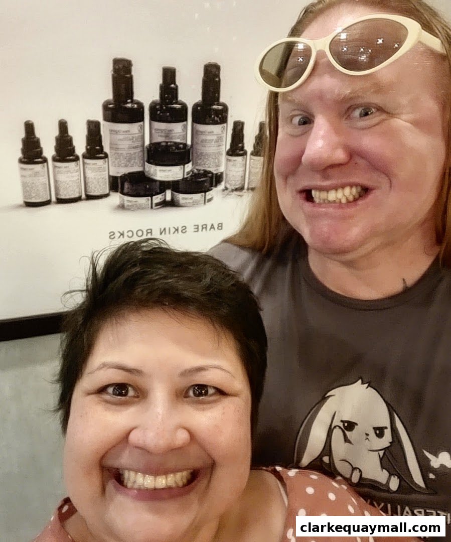 Two smiling people pose in front of a display of organic skincare products.