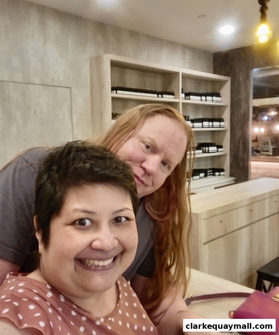 Two smiling people pose for a selfie in front of shelves stocked with skincare products.