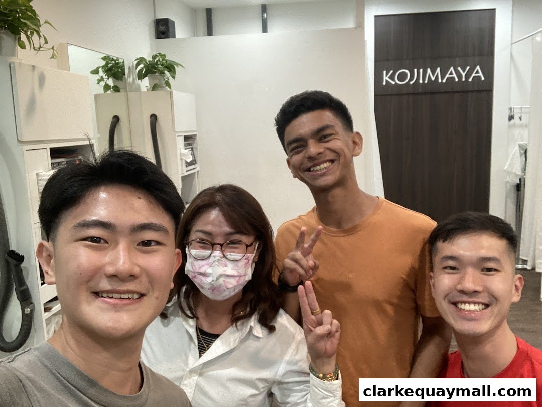 A group of four smiling people pose for a selfie in front of the KOJIMAYA shop sign.