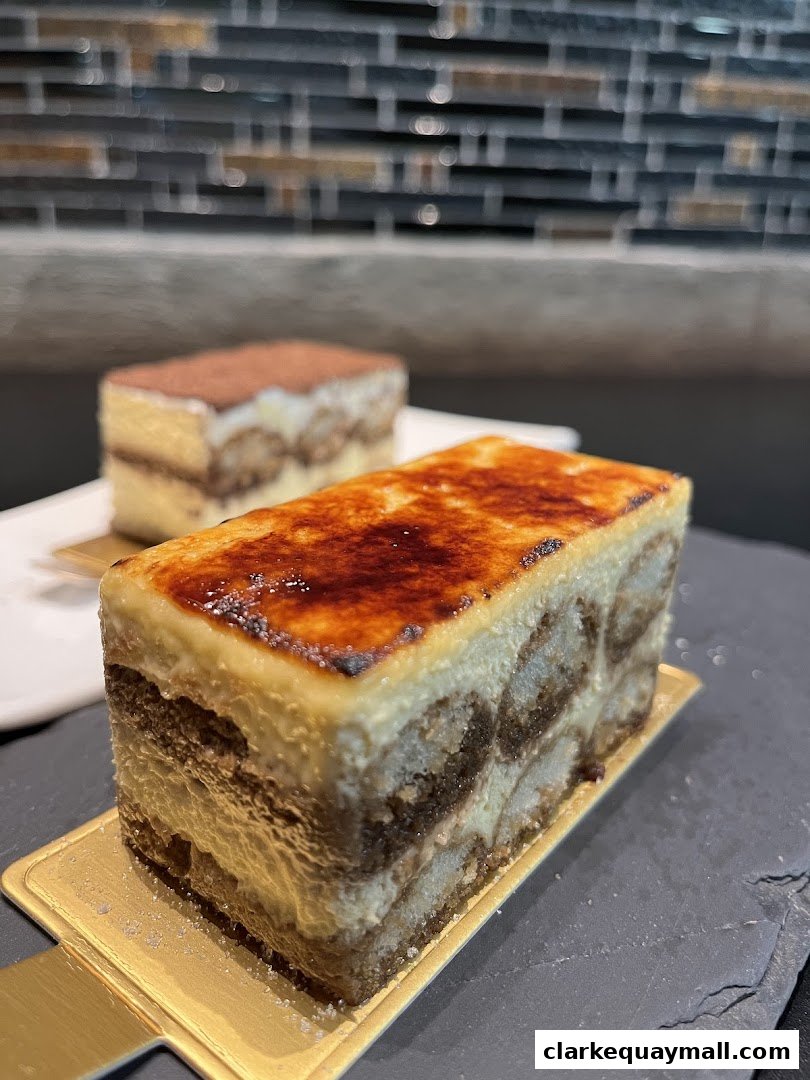 Two delicious tiramisu desserts are presented on a dark slate surface with a blurred tiled background.