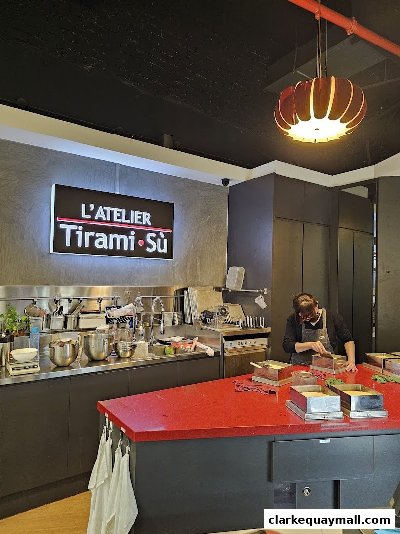 A person works at a red counter in a modern kitchen with a "L'Atelier TiramiSu" sign.