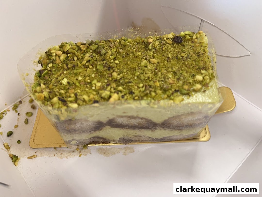 A slice of pistachio tiramisu in a clear plastic container, topped with chopped pistachios.