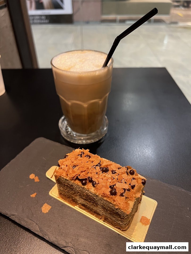 A slice of layered cake with chocolate chips and a frothy coffee drink.