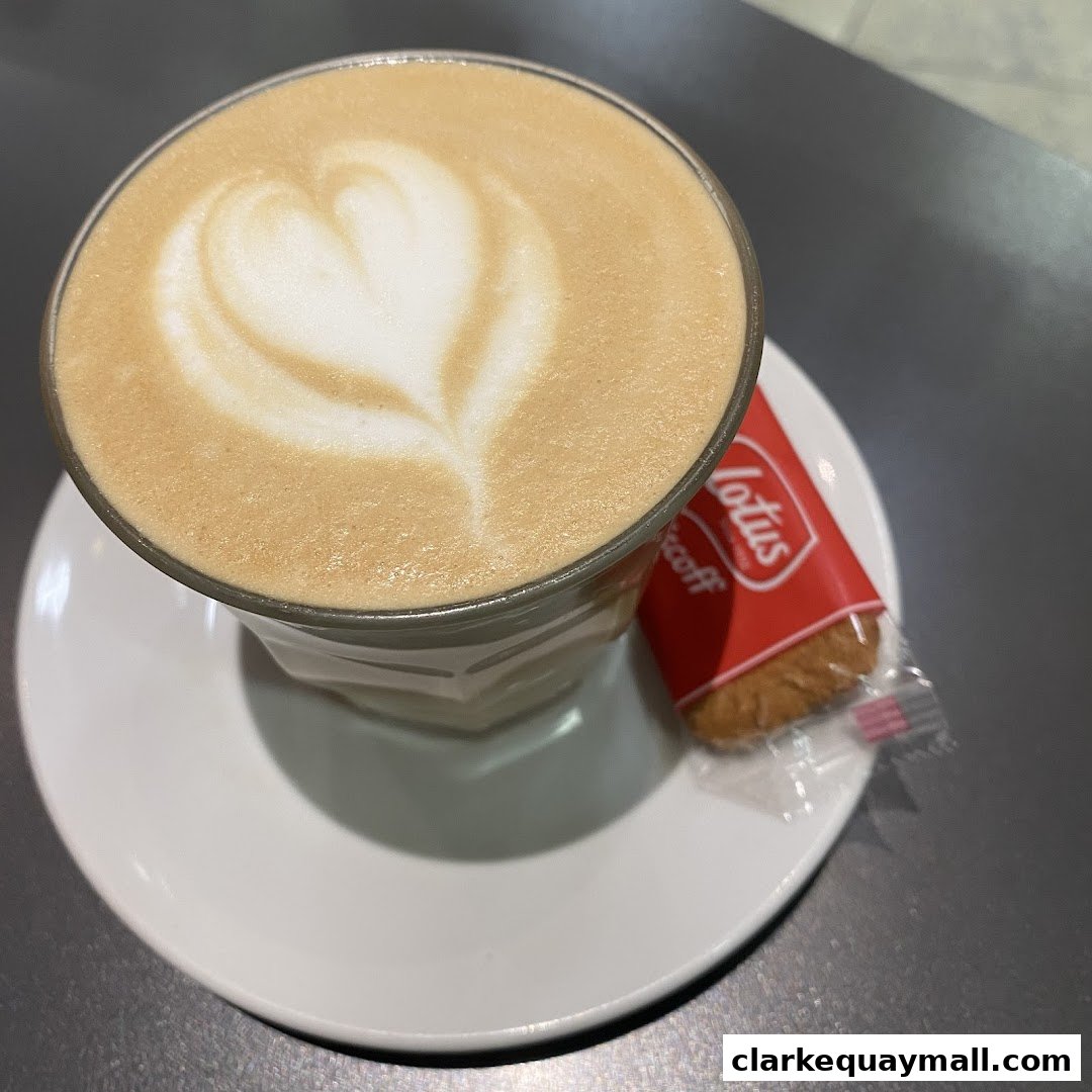A close-up of a latte with heart-shaped foam art and a Lotus Biscoff cookie.