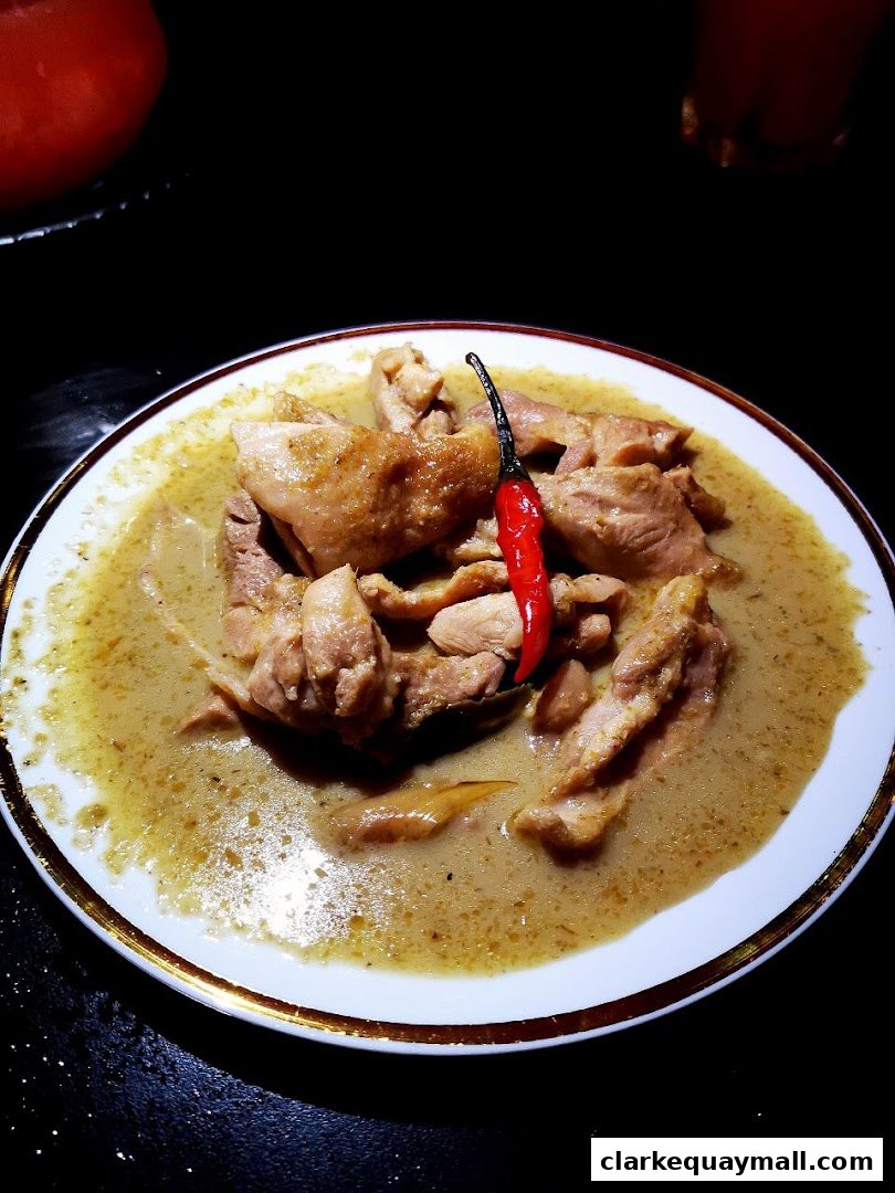 A plate of chicken curry with a red chili on top, served in a restaurant.