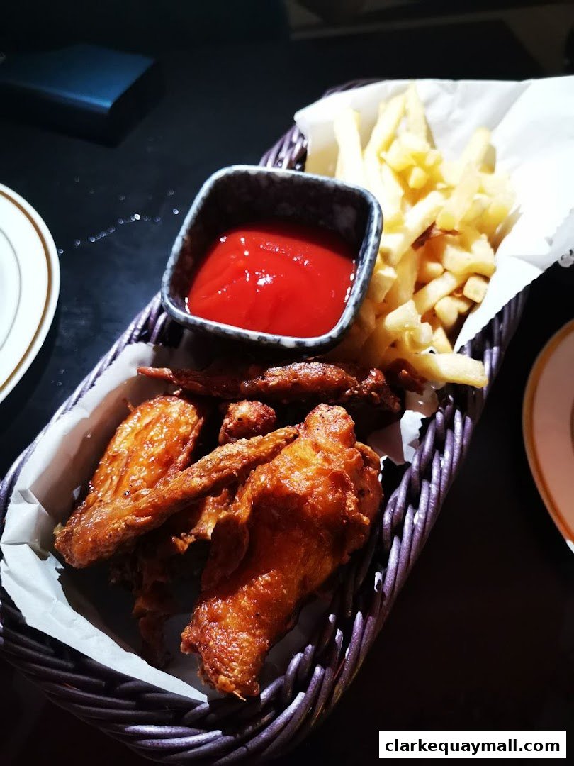 A basket of crispy fried chicken wings and french fries with a side of ketchup.