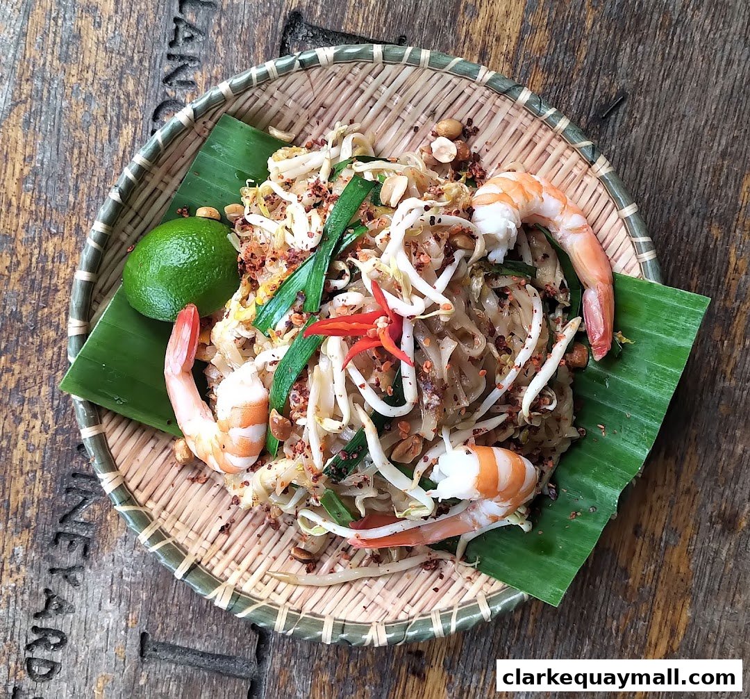 A delicious plate of Pad Thai with shrimp, bean sprouts, lime, and chili on a woven mat.