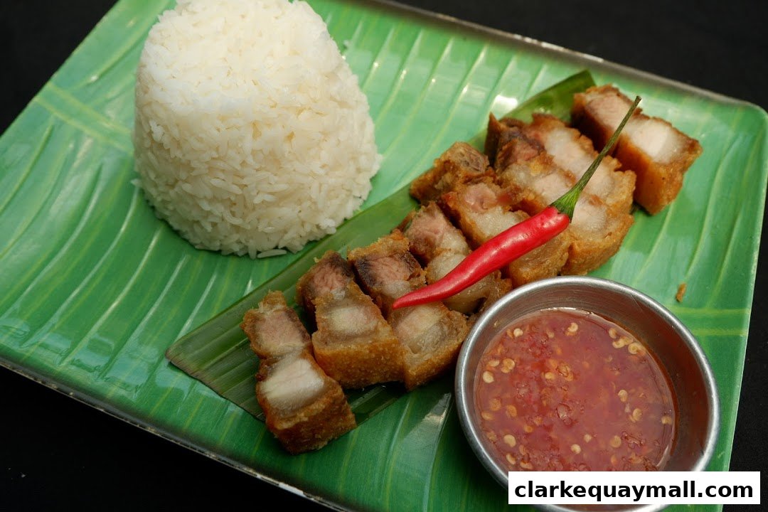 Crispy pork belly with rice and dipping sauce, garnished with a red chili pepper.