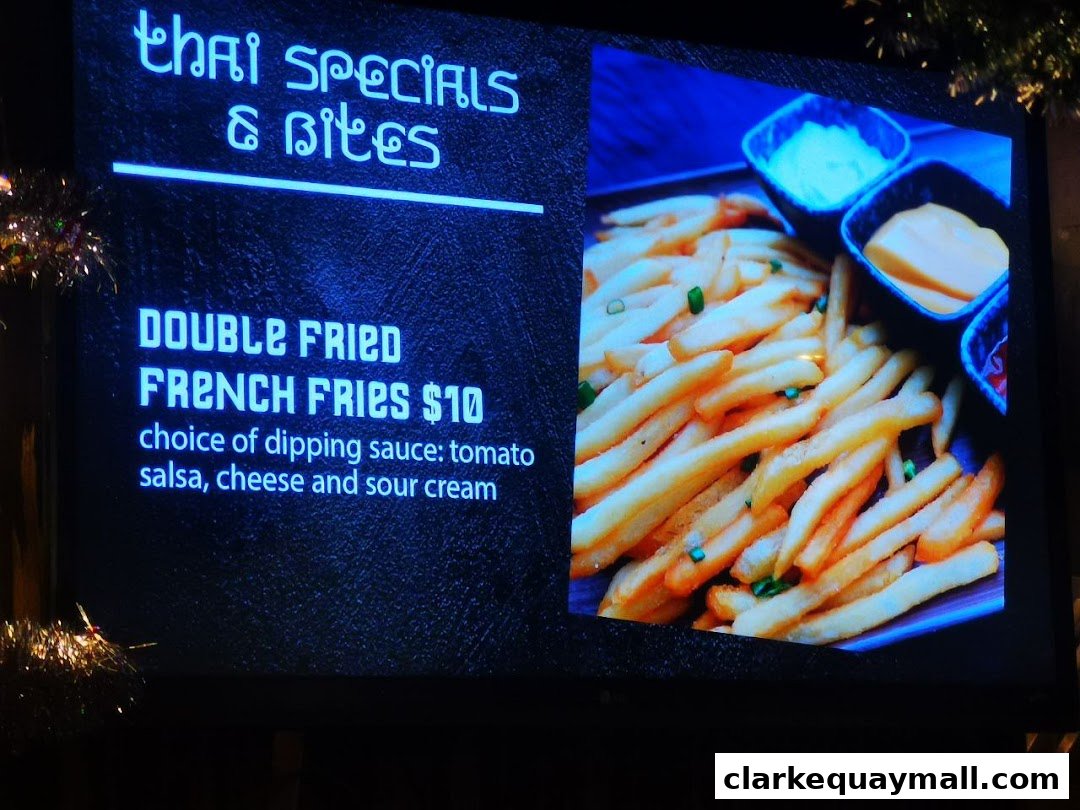 A digital menu board displaying Thai specials and a description of double-fried French fries.