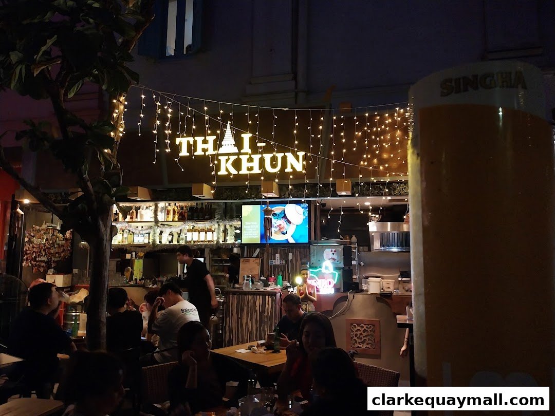 A lively bar scene at night with people dining and a prominent "THAI-KHUN" sign.