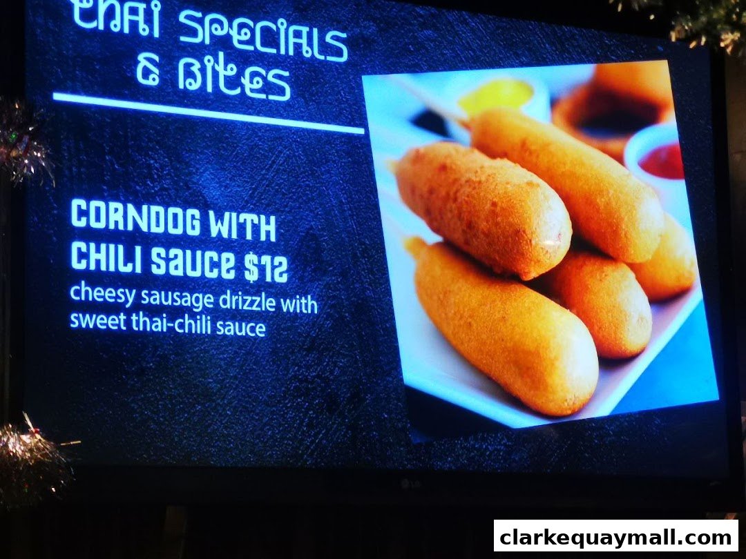A digital menu board displaying Thai specials, featuring corndogs with chili sauce.