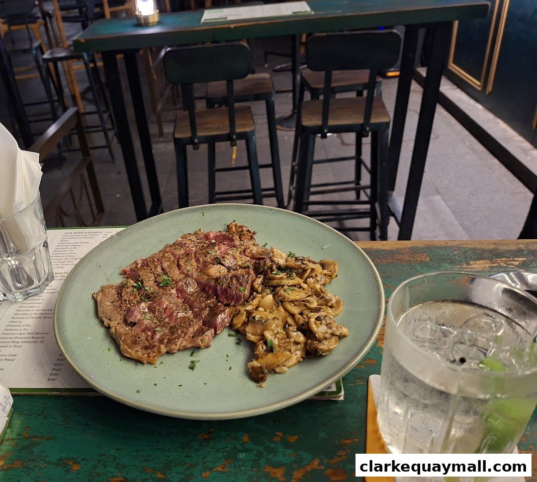A plate of sliced steak with mushrooms and a drink on a wooden table at Lil Dublin Bar.