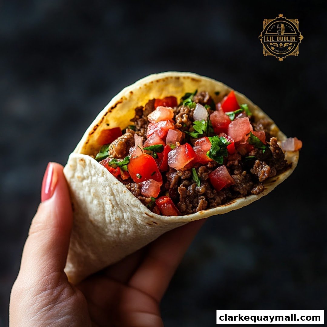 A hand holds a delicious taco filled with seasoned ground beef, diced tomatoes, and onions.