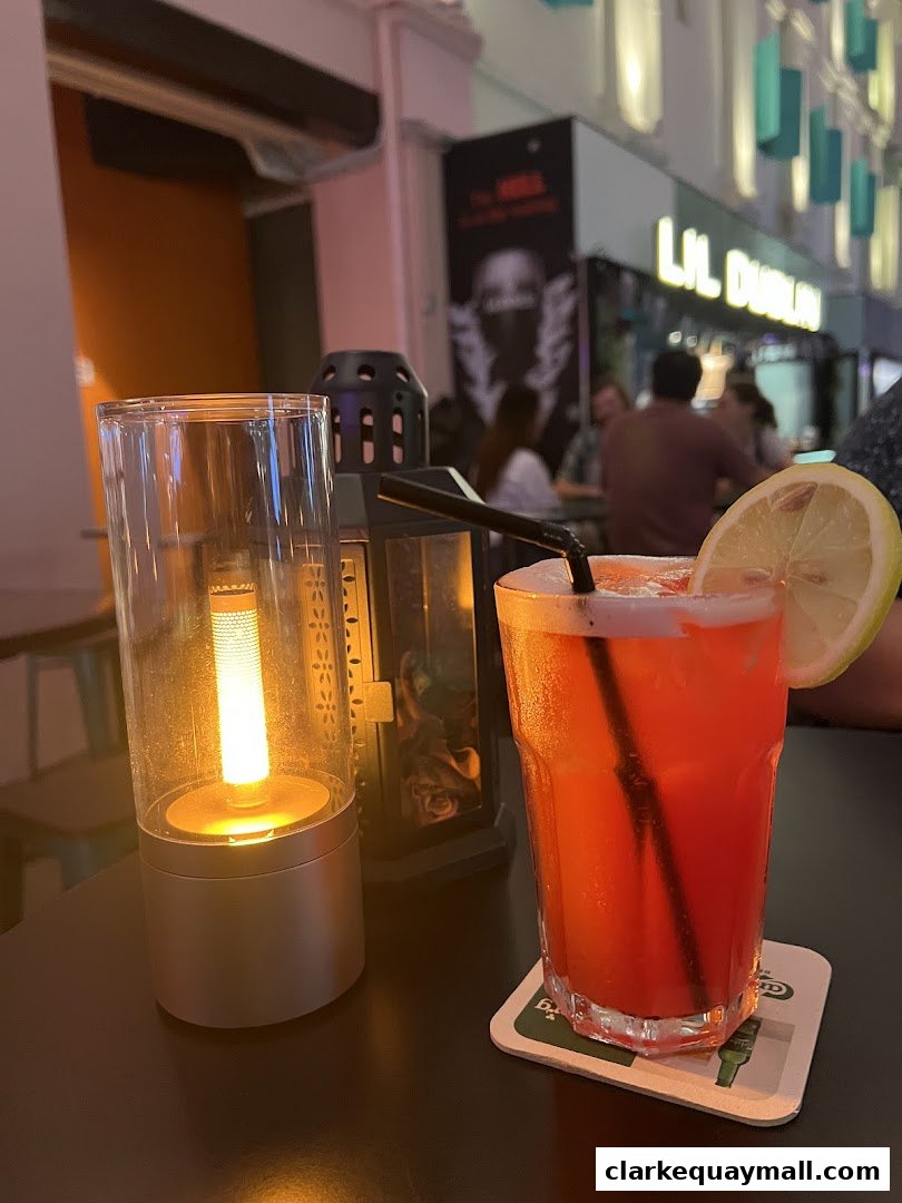 A close-up of a red cocktail with a lemon slice and a decorative lamp on a table.