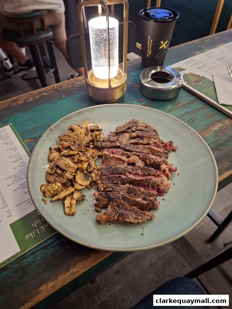 A plate of sliced steak and mushrooms sits on a rustic table with a lamp and coffee cup.