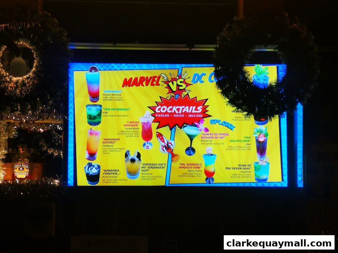 A digital menu board displaying Marvel vs. DC themed cocktails with colorful drinks and descriptions.
