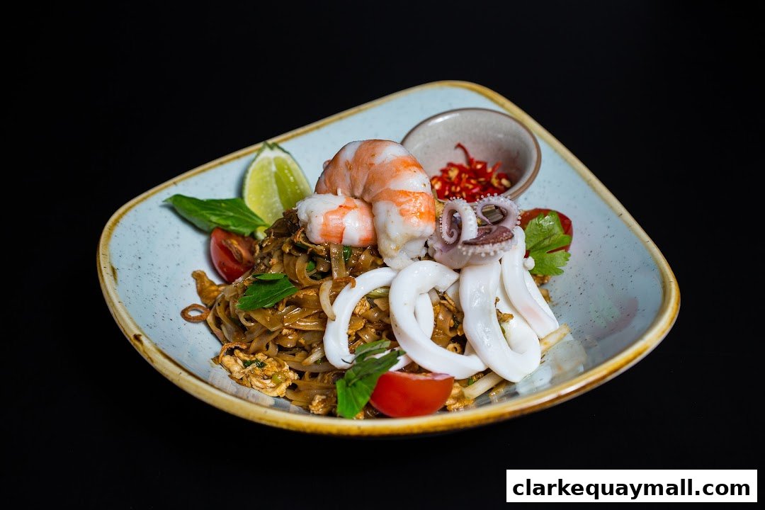 A plate of Pad Thai noodles topped with shrimp, squid, and octopus, garnished with lime and chili.