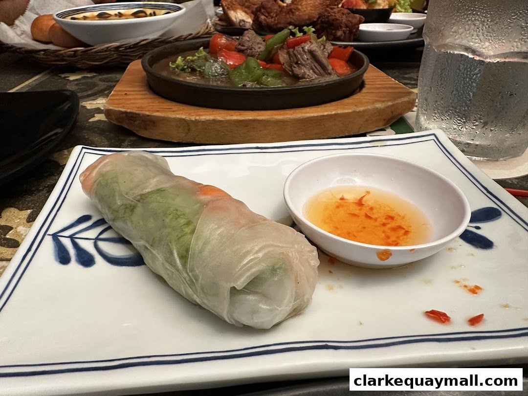 A fresh spring roll with dipping sauce and other Vietnamese dishes on a table.
