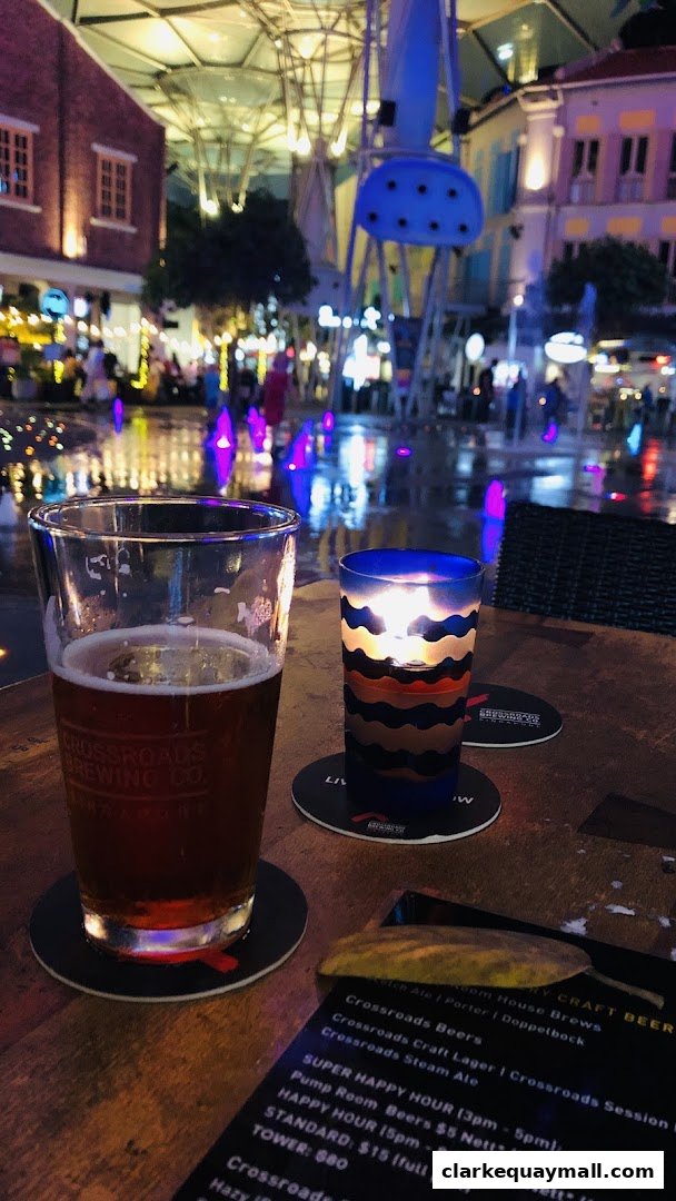 A table with a beer, a candle, and a menu at an outdoor venue with fountains.