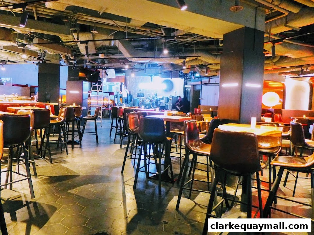 Interior of a bar with high tables and stools, stage with band setup in the background.