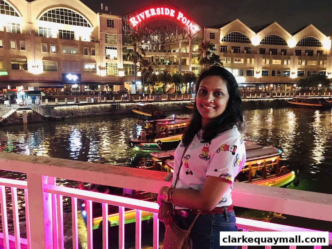 A woman smiles at the camera with a scenic riverside view at night.