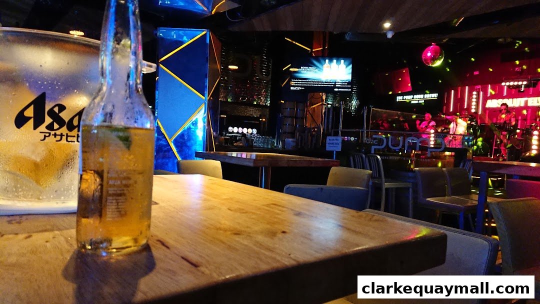 A table in a bar with a bottle of beer and an ice bucket, with a band playing on stage in the background.