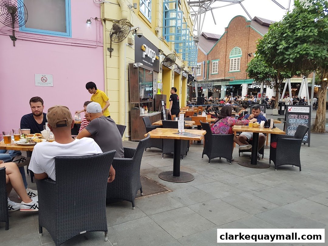 People dining at outdoor tables in front of a restaurant with a pink wall.