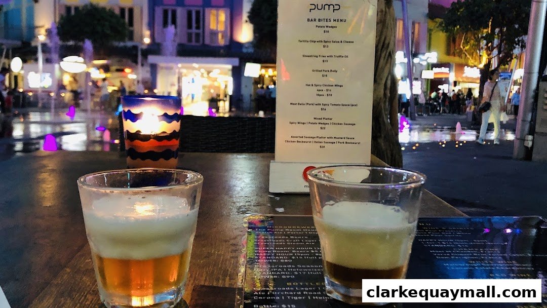 Two drinks on a table with a menu and a candle, with a fountain and shops in the background.