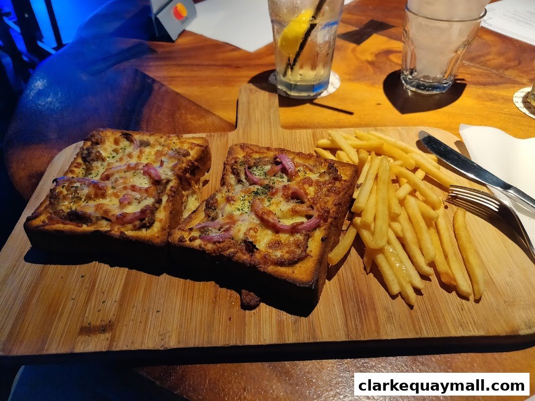 Two open-faced sandwiches with melted cheese and toppings, served with french fries on a wooden board.