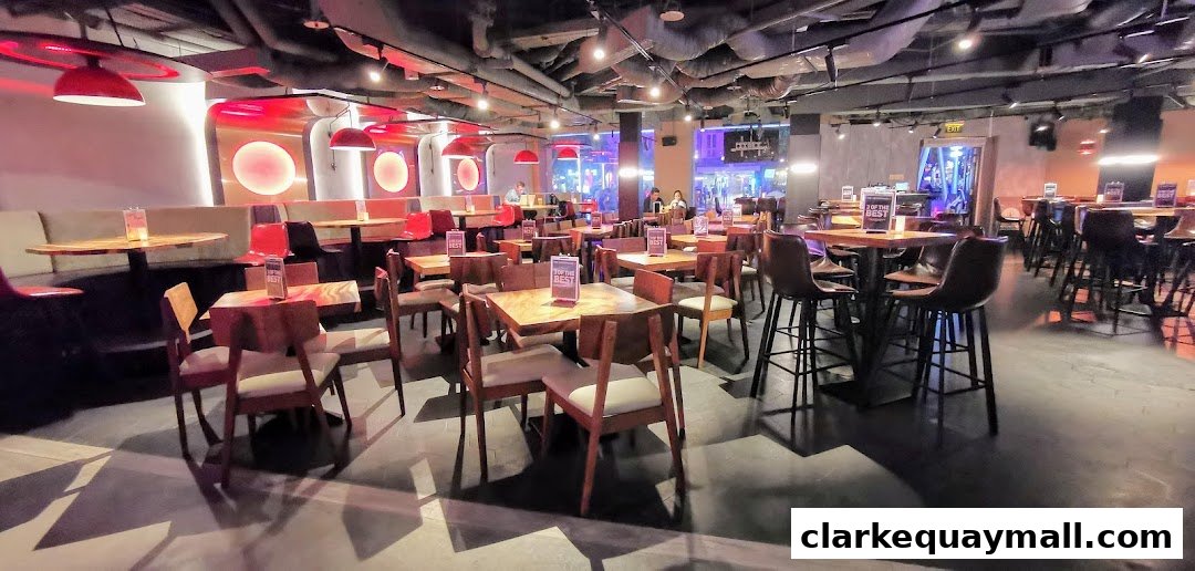 Interior view of a modern restaurant with wooden tables, chairs, and bar stools, illuminated by red lighting.