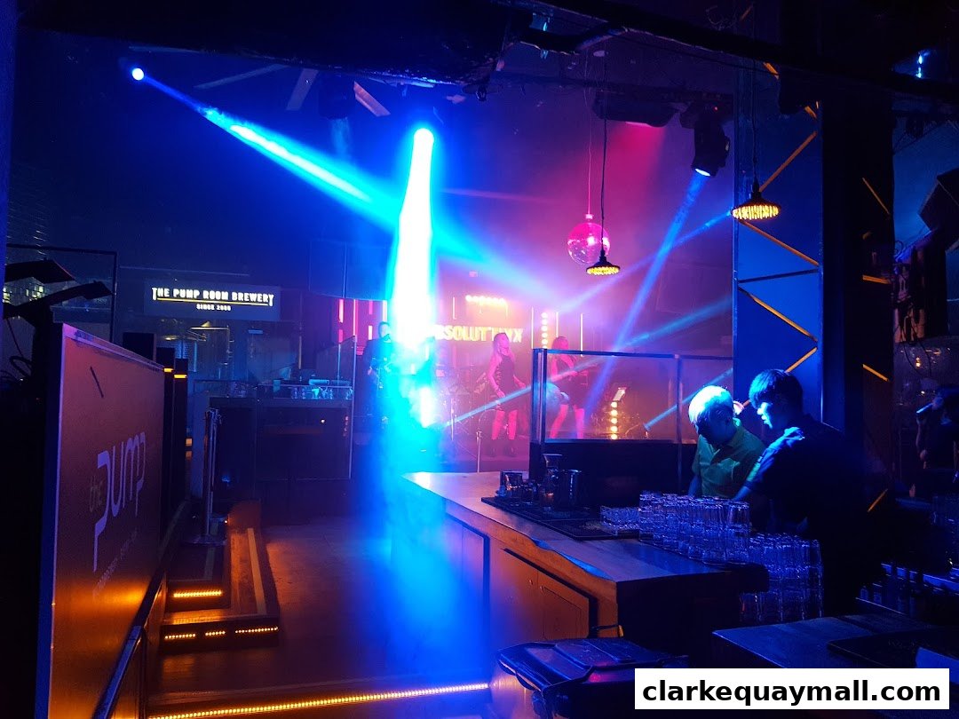 A lively bar interior with a DJ booth, stage, and patrons enjoying the atmosphere.