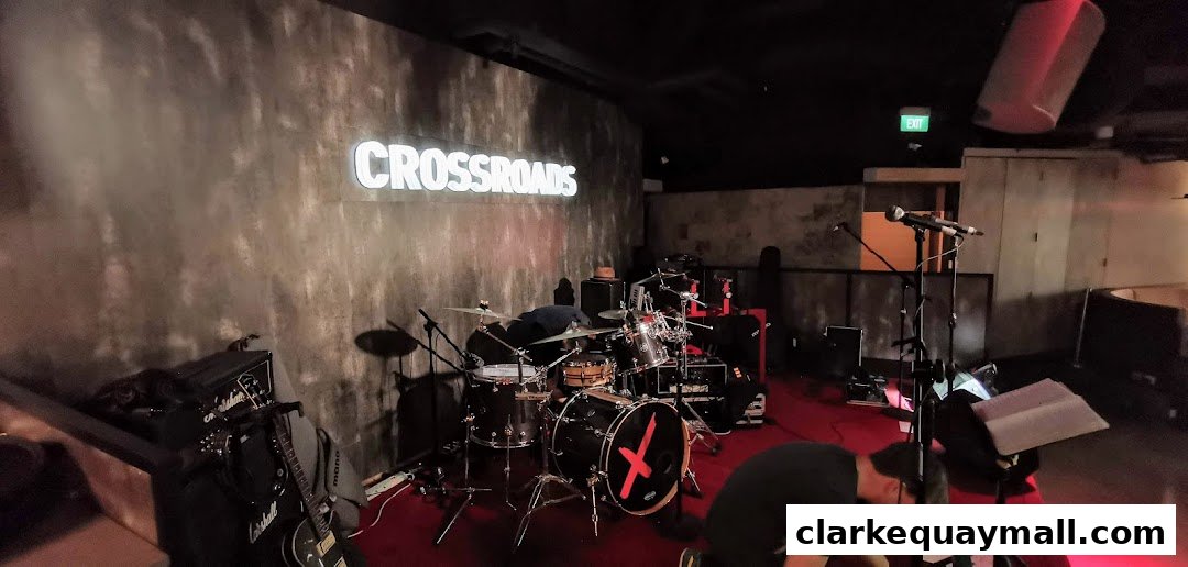A stage setup with a drum kit, guitars, amplifiers, and microphones at a venue called Crossroads.