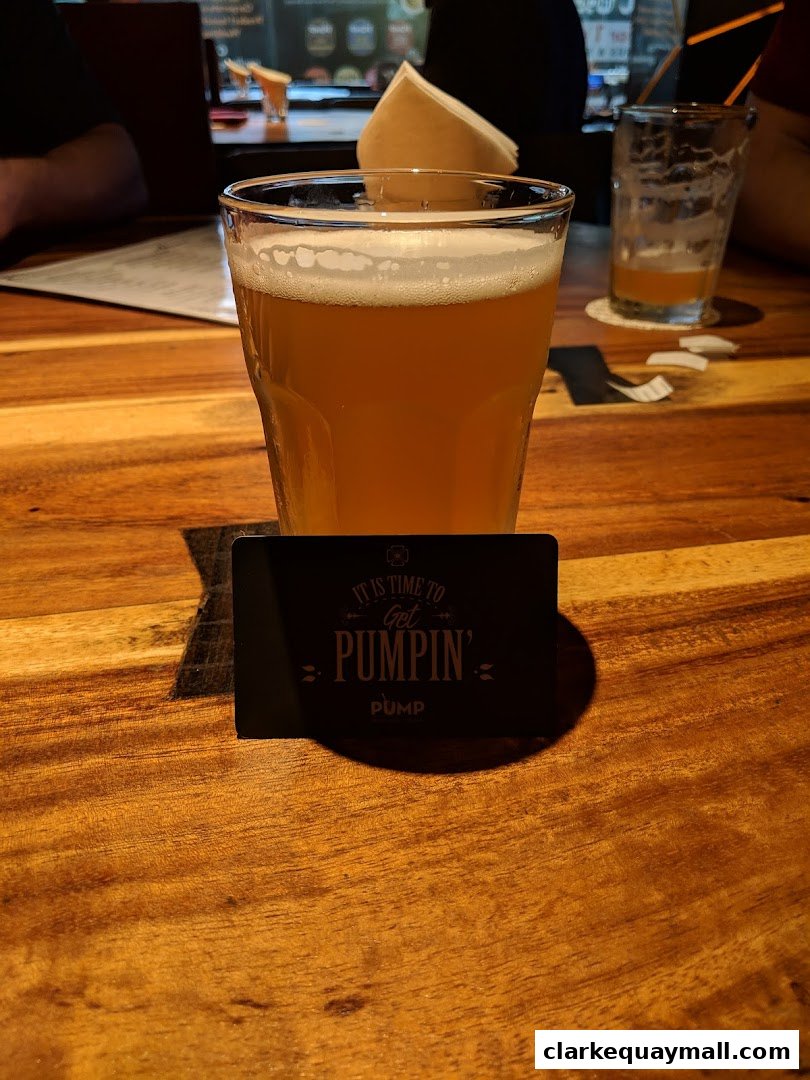A glass of beer sits on a wooden table with a promotional card.