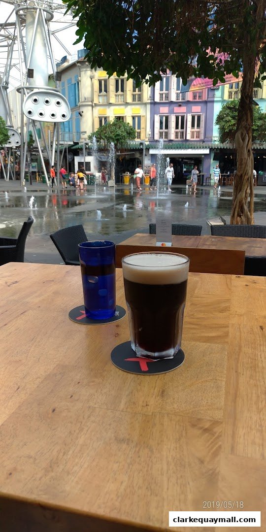 Two drinks on a wooden table with a fountain and colorful buildings in the background.