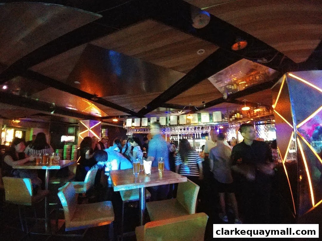 Interior view of a lively bar with people seated at tables and standing near the bar.