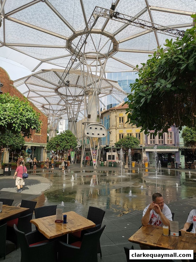 Outdoor seating area with fountains and shops in the background.