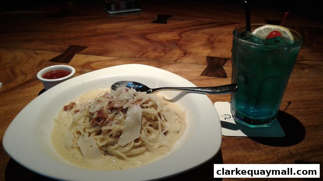 A plate of spaghetti carbonara and a blue cocktail with cherry and lemon garnish.