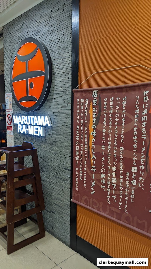 The entrance of Marutama Ramen features a prominent logo and illuminated signage.
