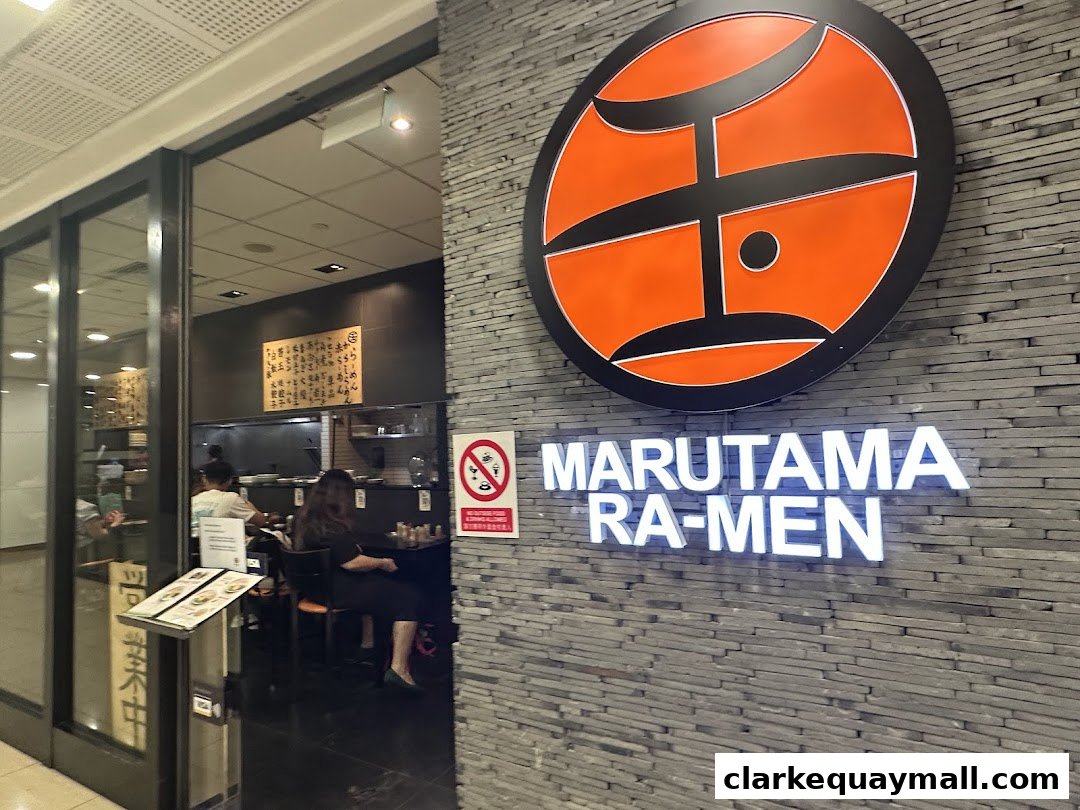 The entrance to Marutama Ramen, featuring its logo and illuminated sign on a stone wall.